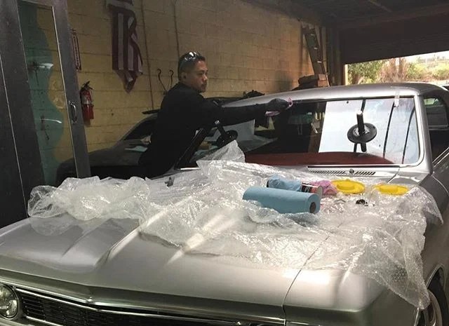 Technician installing a new windshield on a classic car in a garage using a suction cup tool